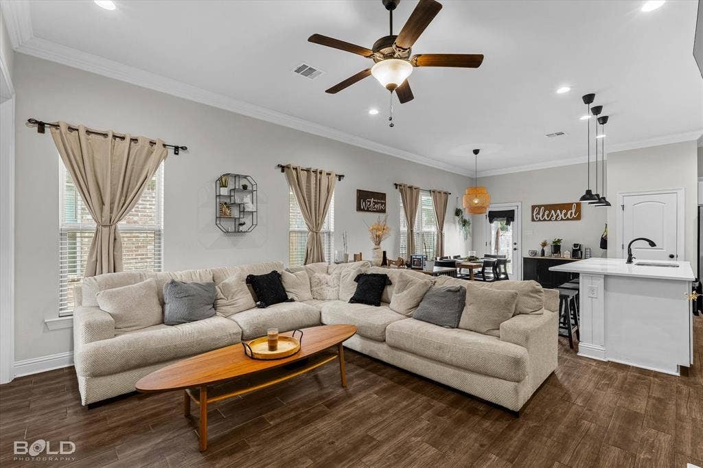 Wood-finish flooring throughout, crown molding, ceiling fan with integrated lighting, recessed lighting, and a kitchen island with pendant lighting