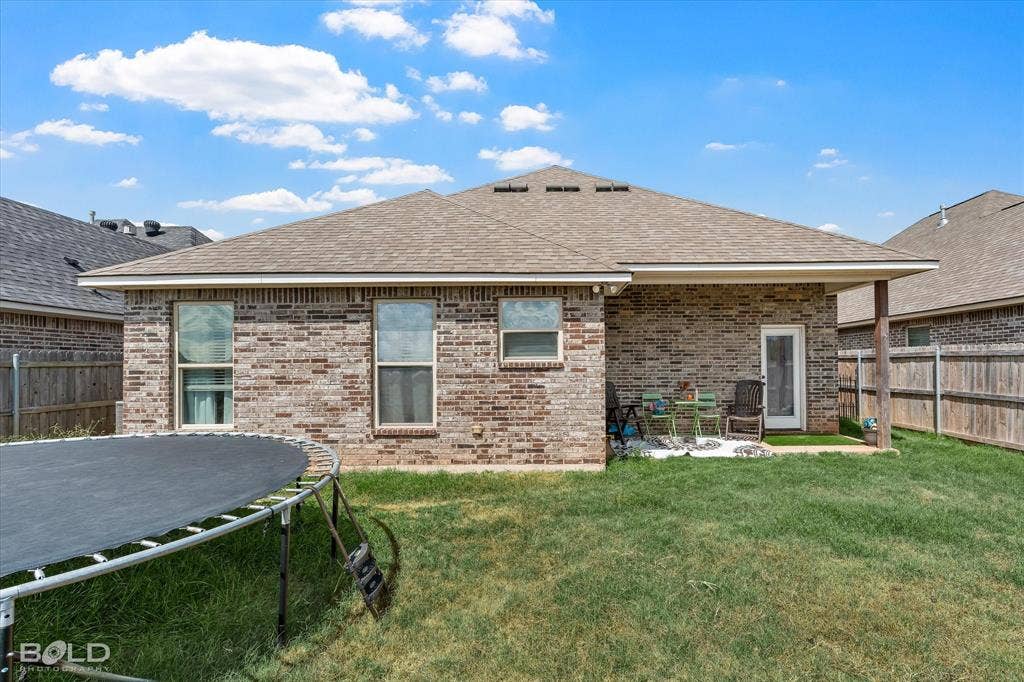 Brick exterior with multiple windows, covered patio, wood support columns, and privacy fencing