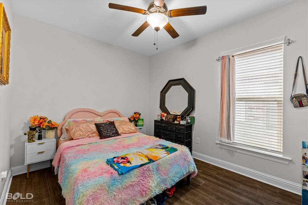 Wood-finish flooring, ceiling fan with integrated lighting, window with blinds, and white trim throughout