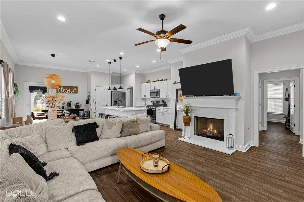 Open-concept living space featuring wood-finish flooring, a white mantel fireplace, and a ceiling fan