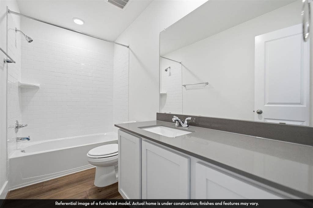 5218 Noland Drive, Princeton, TX 75071 Bathroom featuring a vanity with a solid-surface countertop, an undermount rectangular sink, wood-finish flooring, a full-width wall mirror, and a tub-shower combination with tiled walls