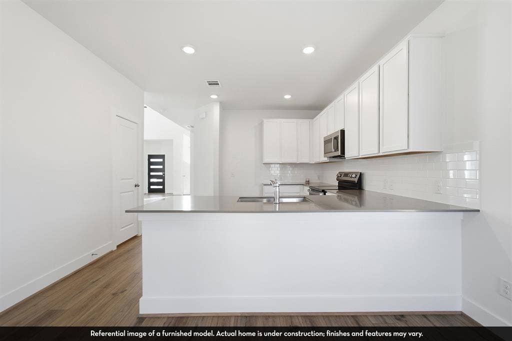 821 Whitmore Drive, Princeton, TX 75071 Kitchen featuring white shaker-style cabinetry, neutral solid-surface countertops, white subway tile backsplash, recessed ceiling lighting, and wood-finish flooring