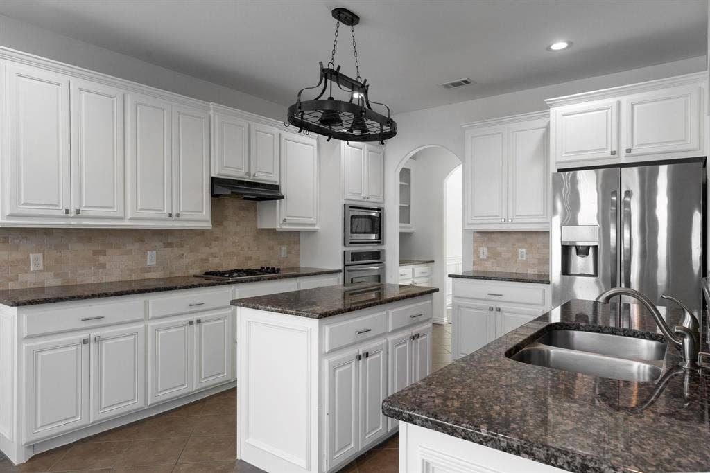White cabinetry, stainless steel appliances, stone countertops, a tile backsplash, and a central kitchen island
