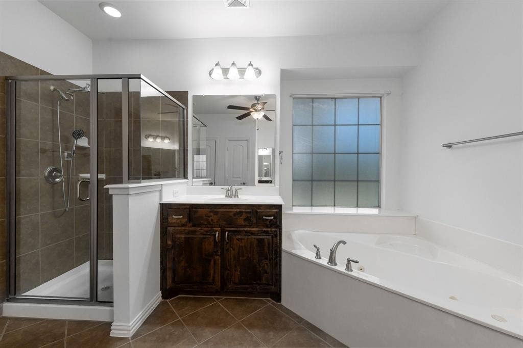 Corner soaking tub, separate glass-enclosed shower with tile surround, single vanity with dark wood-finish cabinetry, and tiled flooring