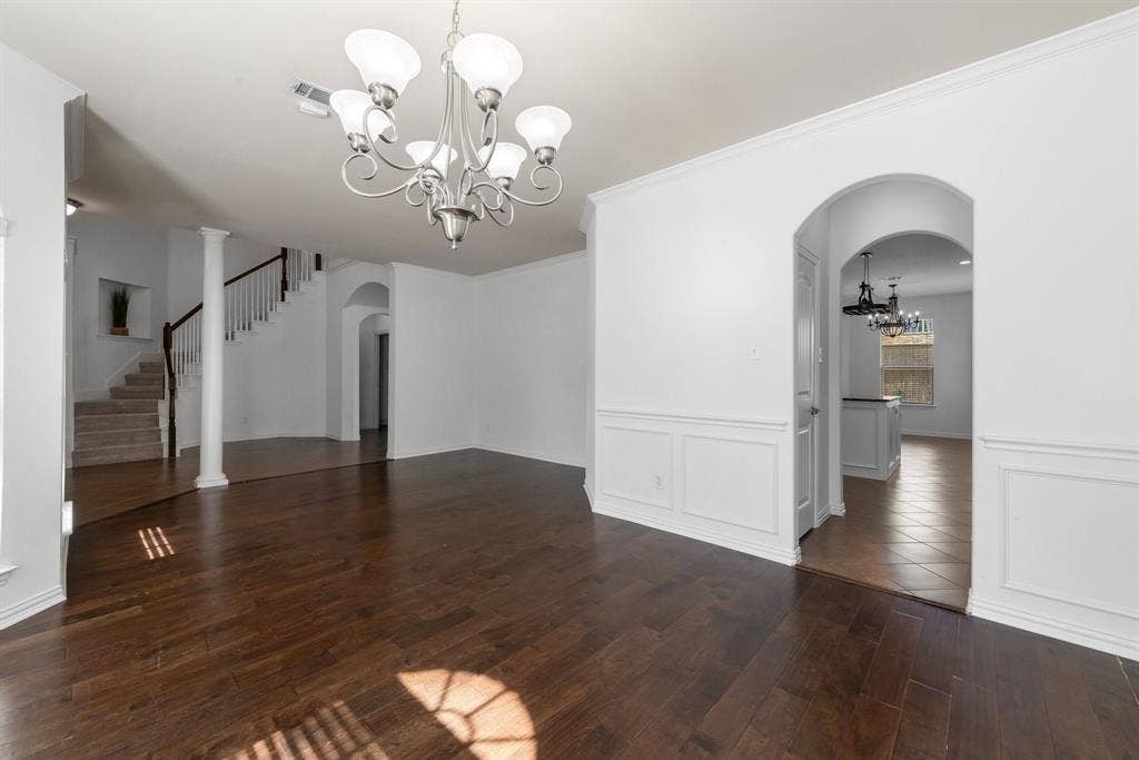 Wood-finish flooring with crisp white walls, extensive crown molding, a built-in staircase, and an archway