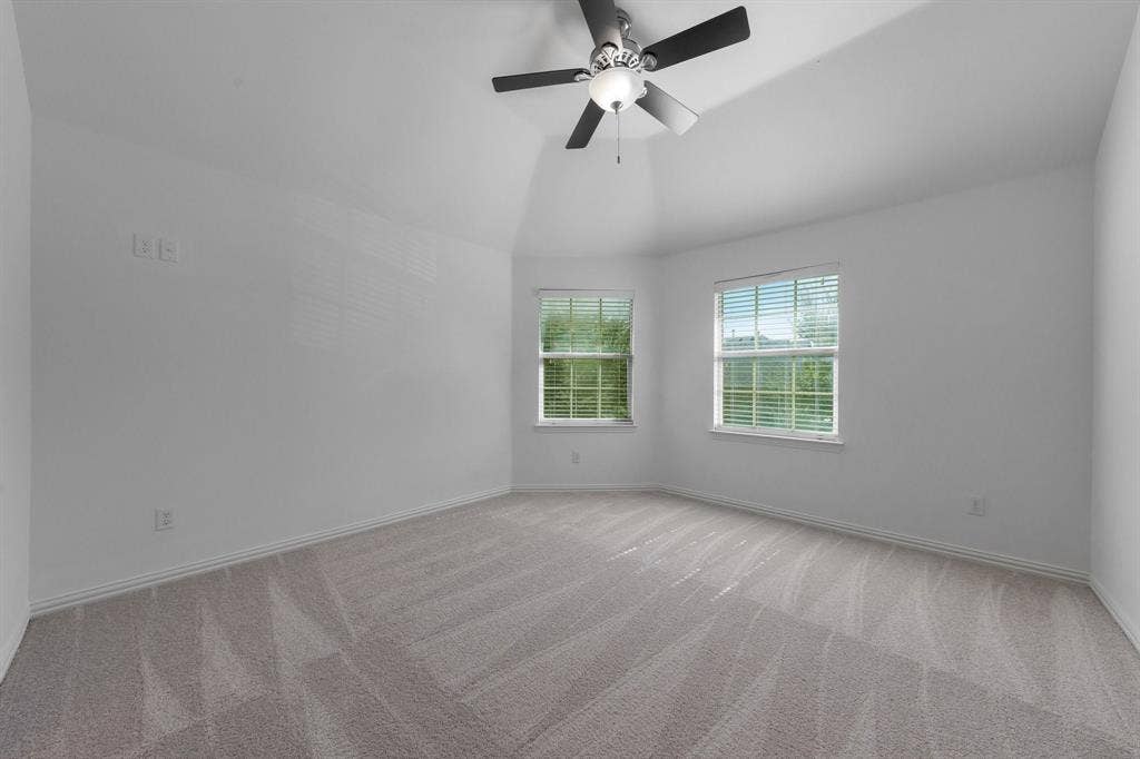 Vaulted ceiling with a ceiling fan, two windows, wall-to-wall carpeting, and white wall finishes