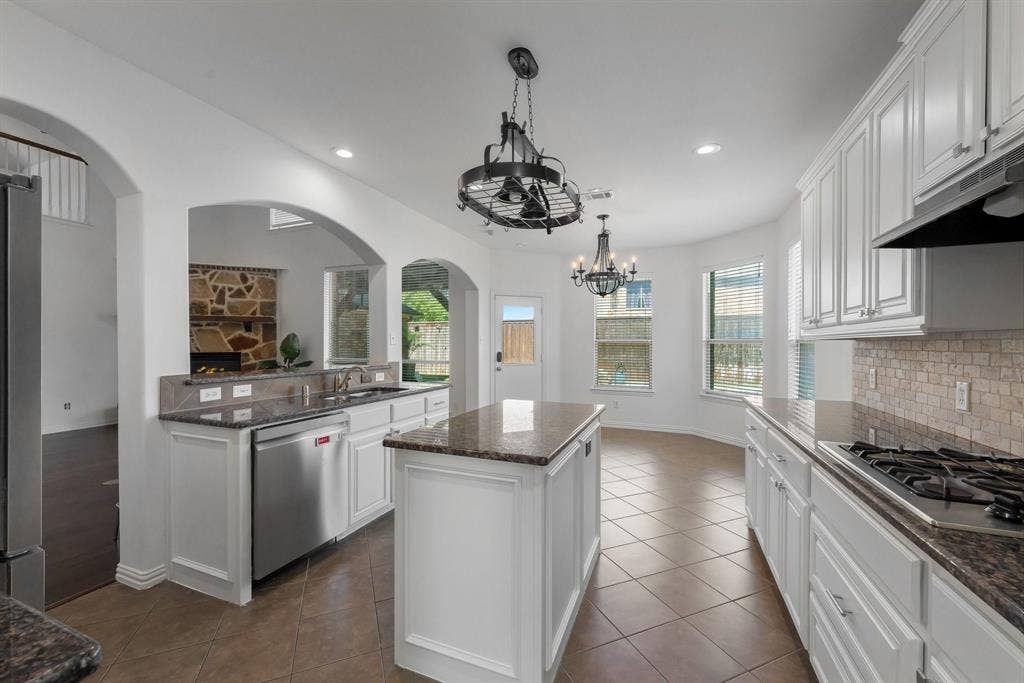 Kitchen featuring white cabinetry, stone countertops, a central island, tile flooring, and integrated stainless steel appliances