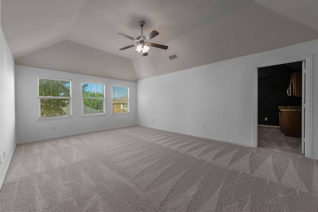 Spacious room featuring a vaulted ceiling with a ceiling fan, three windows, and patterned carpet flooring