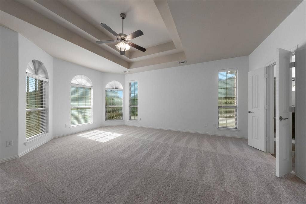 Spacious Master bedroom with tray ceiling, ceiling fan with light, multiple arched windows, and brand new carpet