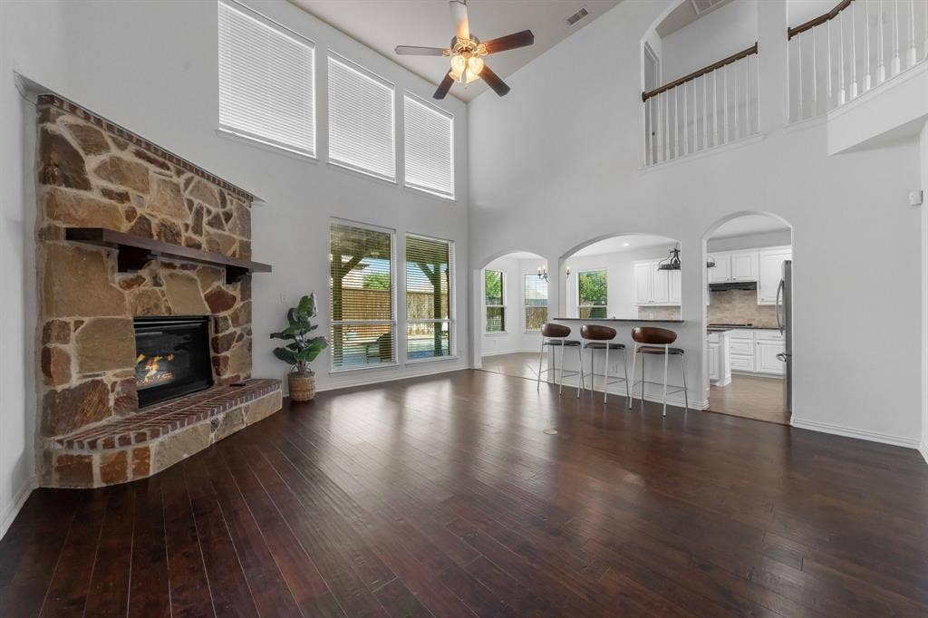 Vaulted ceilings with a ceiling fan, stone fireplace with a wood mantle, rich wood-finish flooring, and arched doorways