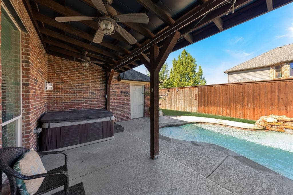 Covered patio featuring a ceiling fan, hot tub stays with the home, and concrete flooring