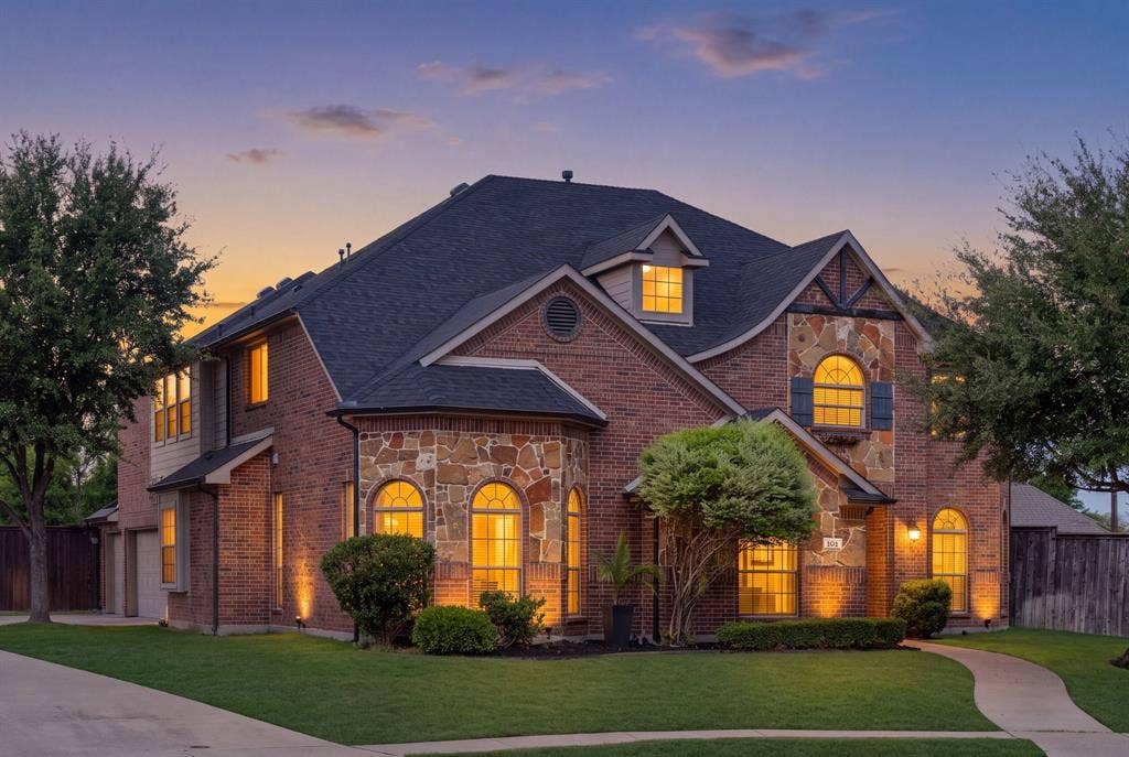 Brick and stone exterior with arched windows, gabled roofline, dormer windows, and established landscaping