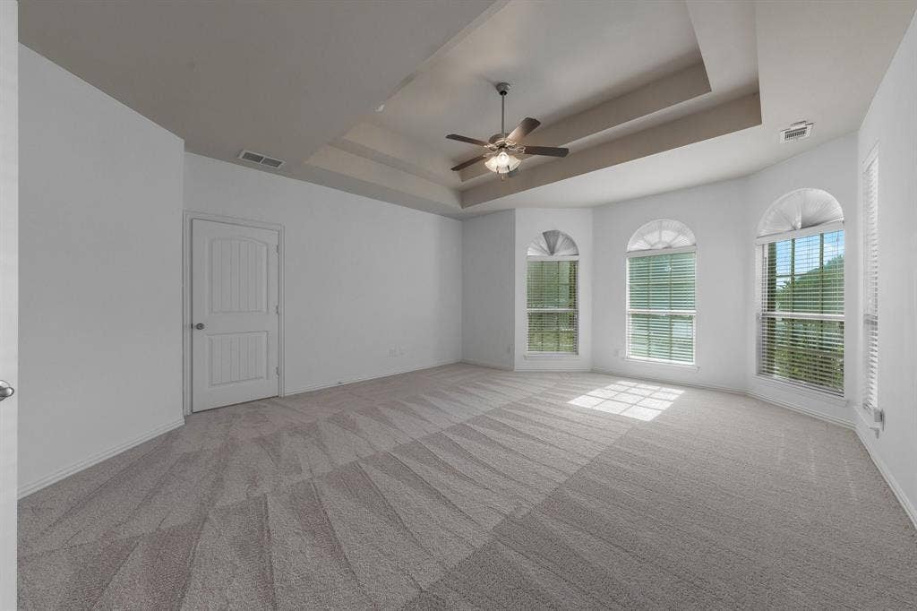 Tray ceiling with a ceiling fan, three arched windows, wall-to-wall carpeting, and a paneled interior door