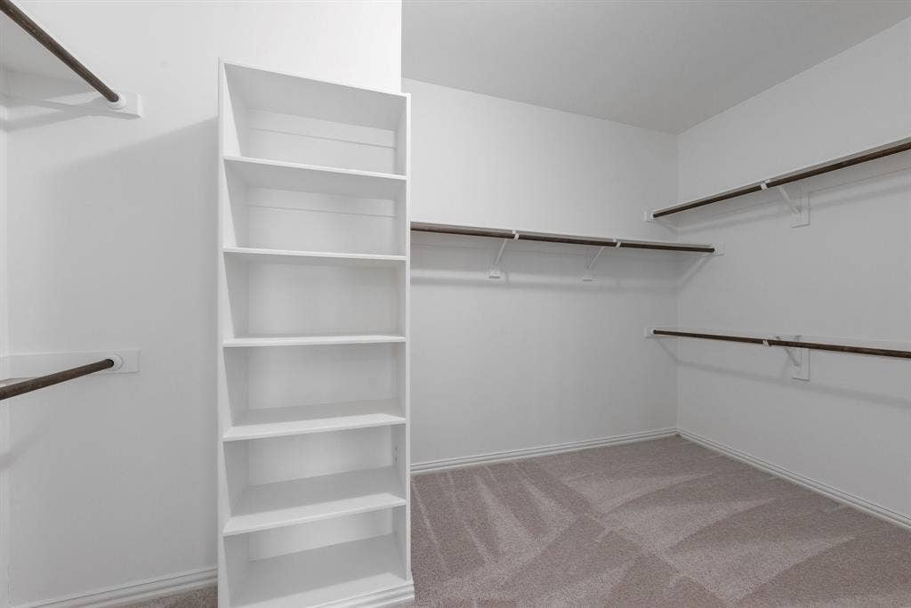 Built-in shelving unit, multiple clothing rods, light-toned carpeting, and painted walls