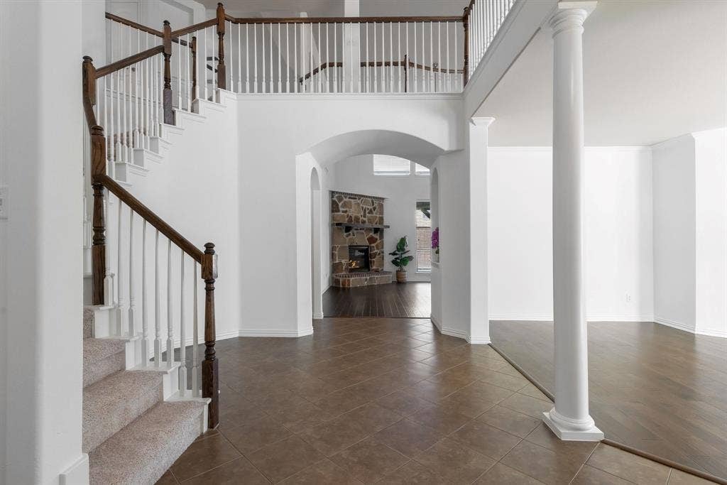 Two-story foyer featuring a curved staircase with wood-finish handrails, a second-story open landing, and a decorative column