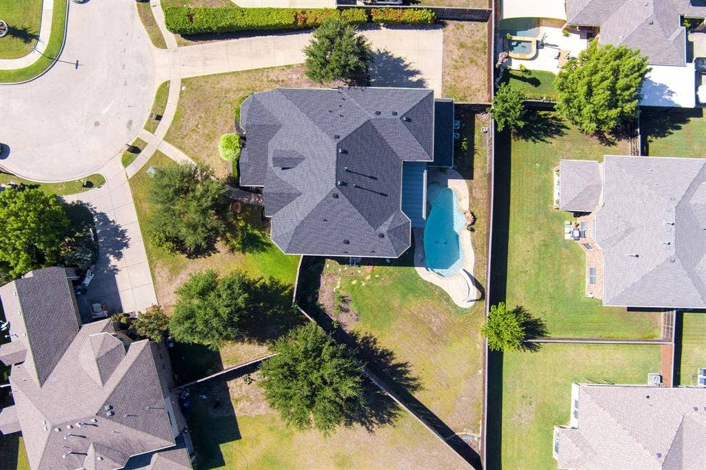 Expansive property featuring a curved swimming pool, dark shingle roof, and mature perimeter trees