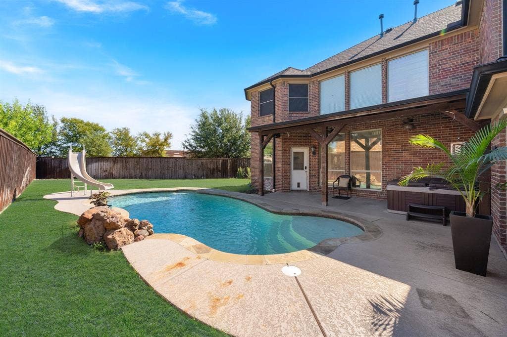 Brick exterior with a covered patio featuring a built-in spa, an in-ground swimming pool, and a fenced backyard with mature trees