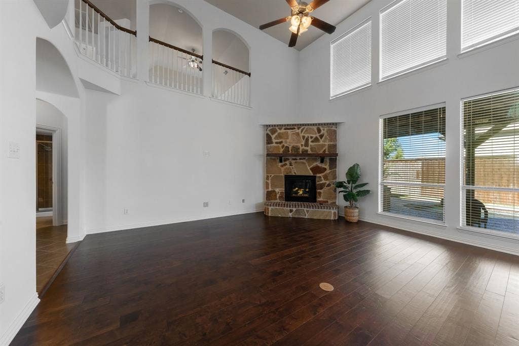 Vaulted ceiling with a ceiling fan, stone fireplace with a wood mantel, dark wood-finish flooring, and multiple large windows