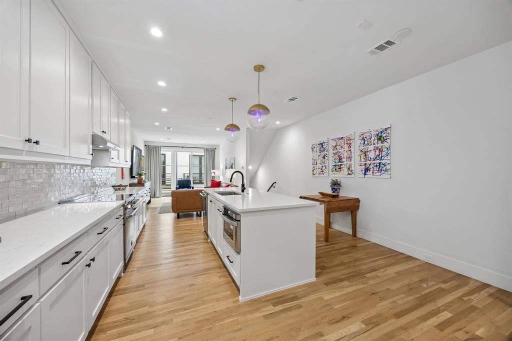 7207 Gaston Avenue, #903, Dallas, TX 75214 Kitchen featuring white cabinetry, light oak wood flooring, a center island with built-in appliances, and a tiled backsplash