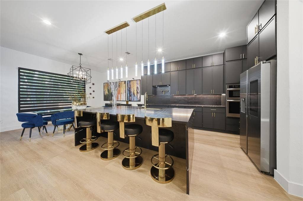522 S Clark Road, Cedar Hill, TX 75104 Sleek kitchen featuring dark cabinetry, stainless steel appliances, a large island with pendant lighting, light wood-finish flooring, and a dining area with a geometric chandelier