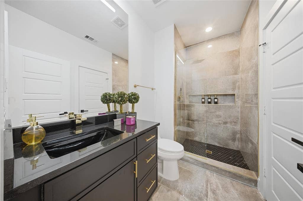 522 S Clark Road, Cedar Hill, TX 75104 Spacious bathroom featuring a dark vanity with gold-tone hardware, a black vessel sink, and a glass-enclosed shower with tiled walls and a recessed niche
