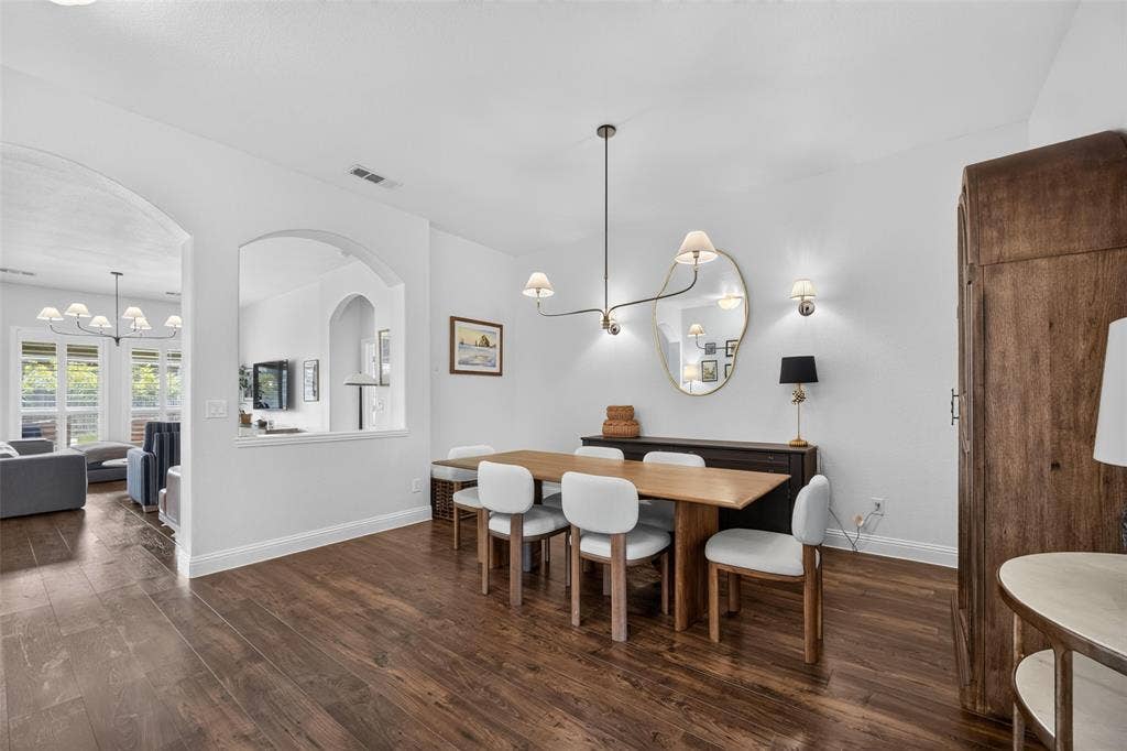 3210 Creekhaven Drive, Melissa, TX 75454 Dining area featuring wood-finish flooring, an arched wall cutout, a contemporary multi-arm chandelier, and wall-mounted lighting