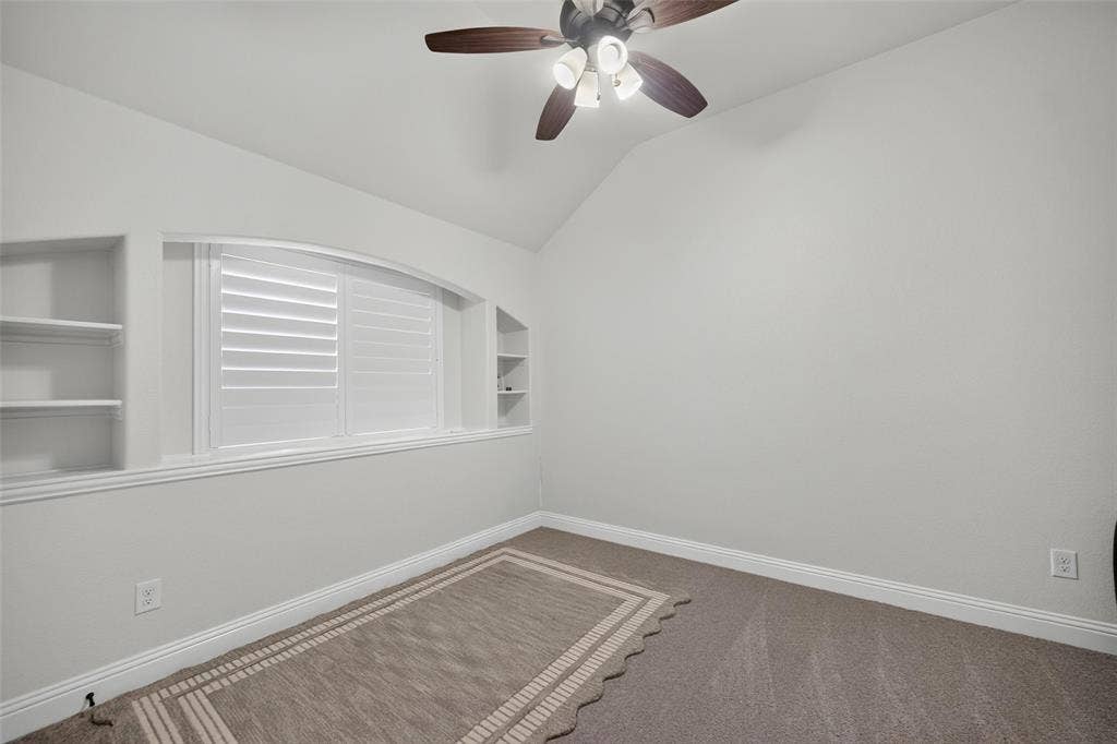 3210 Creekhaven Drive, Melissa, TX 75454 Vaulted ceiling featuring a central multi-blade ceiling fan, arched window with plantation shutters, and symmetrical built-in shelving