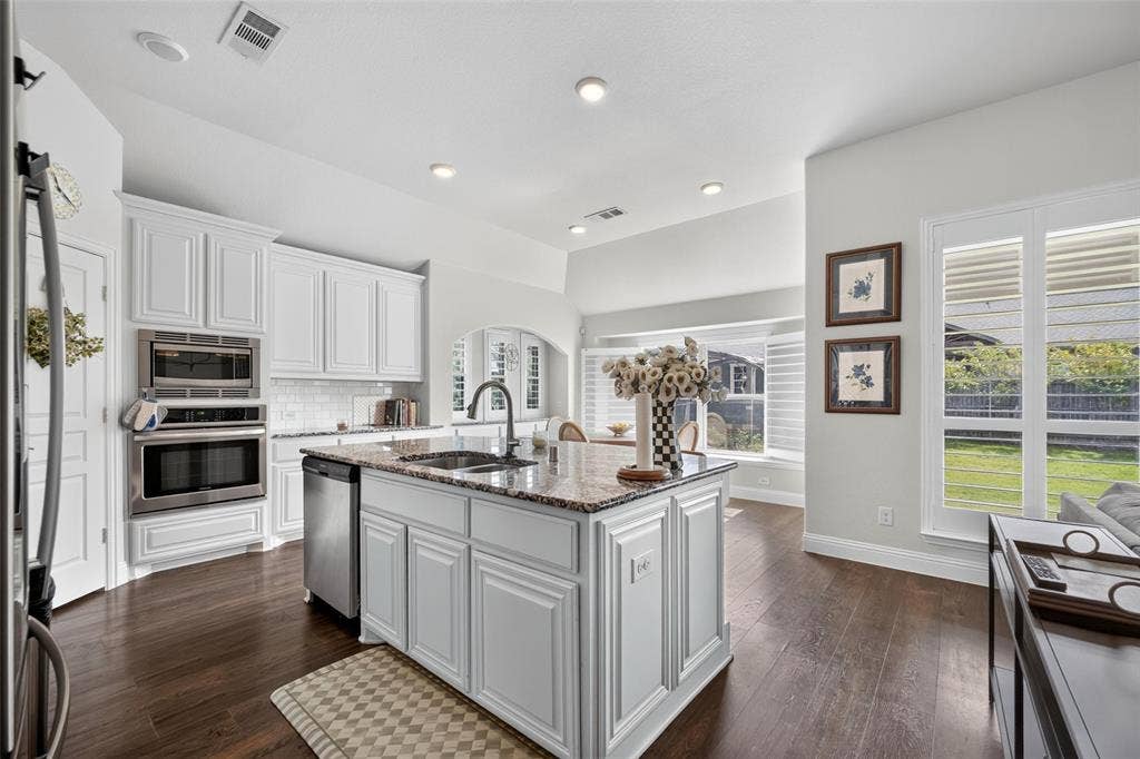 3210 Creekhaven Drive, Melissa, TX 75454 Kitchen featuring white cabinetry, stone-surface island with an undermount sink, built-in wall oven and microwave, and wood-finish flooring