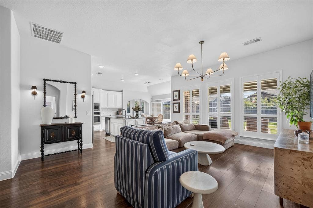 3210 Creekhaven Drive, Melissa, TX 75454 Open-concept interior featuring wood-finish flooring, multi-pane windows with plantation shutters, vaulted ceilings, and a decorative chandelier