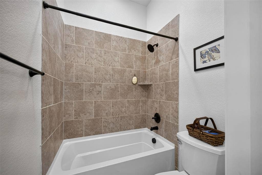 3210 Creekhaven Drive, Melissa, TX 75454 Bathtub enclosure featuring neutral-toned tiled surround, matte black shower head, matching faucet fixture, and integrated soap niche