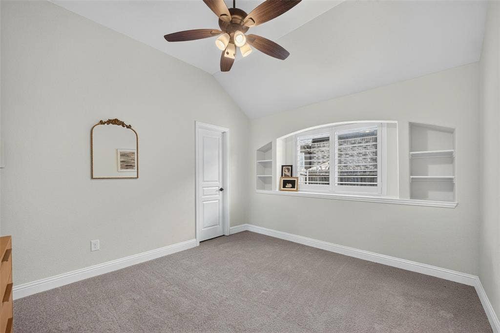 3210 Creekhaven Drive, Melissa, TX 75454 Vaulted ceilings, built-in shelving, arched window recess with shutter treatments, and a central ceiling fan with multi-light fixture