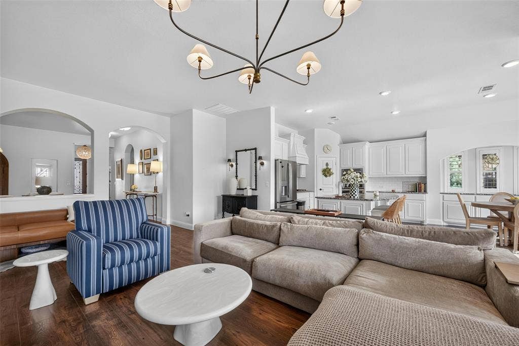 3210 Creekhaven Drive, Melissa, TX 75454 Open-concept interior featuring wood-finish flooring, architectural archways, a multi-arm chandelier, recessed lighting, and kitchen cabinetry with a central island