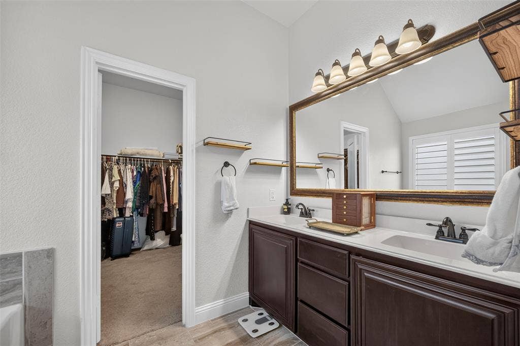3210 Creekhaven Drive, Melissa, TX 75454 Double-sink vanity with dark-finish cabinetry, solid-surface countertop, dual metal faucets, and a large framed vanity mirror with integrated multi-bulb lighting