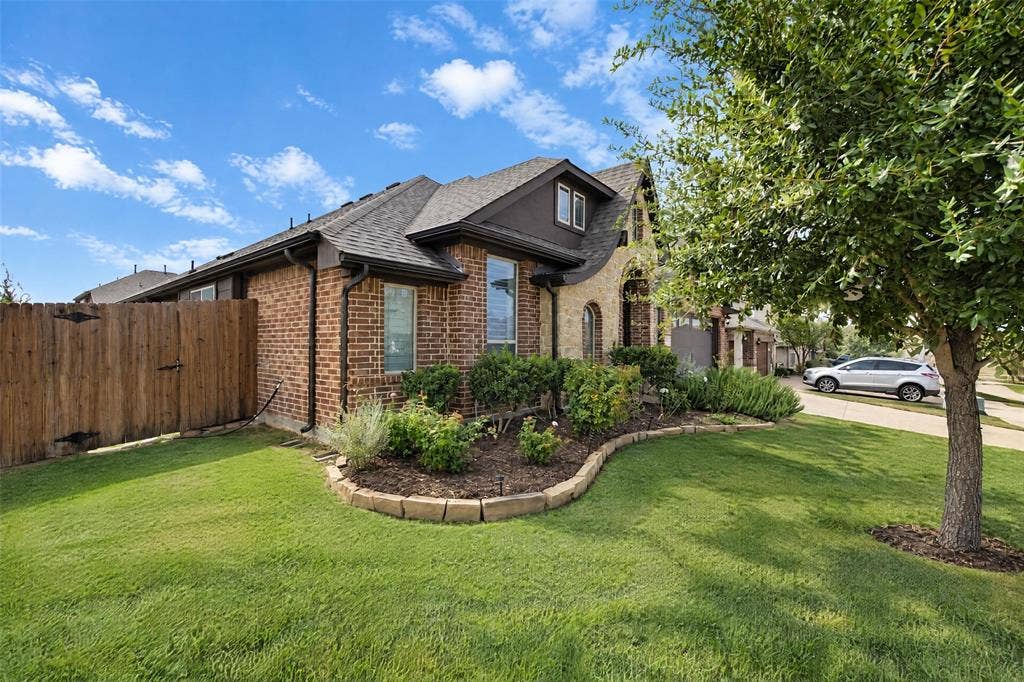 3210 Creekhaven Drive, Melissa, TX 75454 Brick and stone veneer exterior featuring a gabled roofline, manicured lawn, stone-bordered landscape beds, and wood privacy fencing