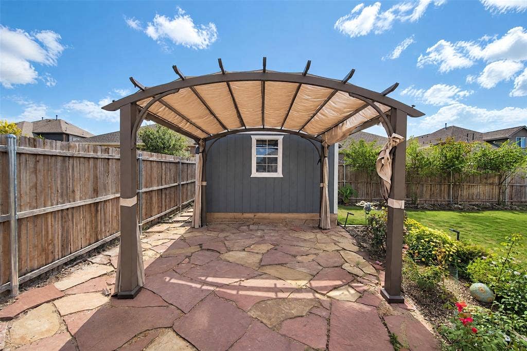 3210 Creekhaven Drive, Melissa, TX 75454 Backyard space featuring a flagstone patio, metal-frame pergola with fabric canopy, and wood-paneled exterior siding