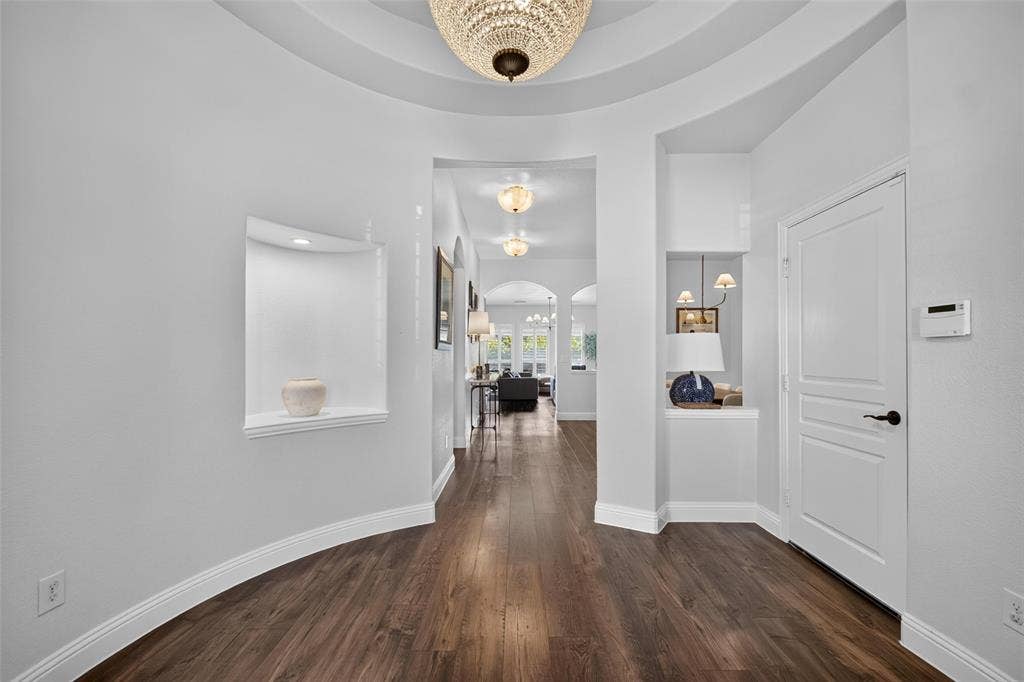 3210 Creekhaven Drive, Melissa, TX 75454 Foyer featuring wood-finish flooring, a tiered tray ceiling with a crystal chandelier, and two recessed wall niches