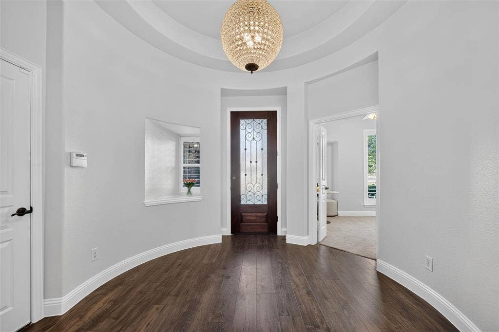 3210 Creekhaven Drive, Melissa, TX 75454 Rotunda entry featuring wood-finish flooring, a domed ceiling, a tiered crystal sphere chandelier, and a wood entry door with wrought iron detailing