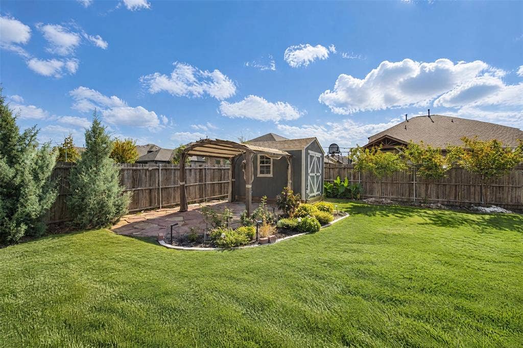 3210 Creekhaven Drive, Melissa, TX 75454 Backyard featuring a manicured lawn, stone-paver patio, wood-frame pergola, storage structure, and perimeter wood privacy fencing