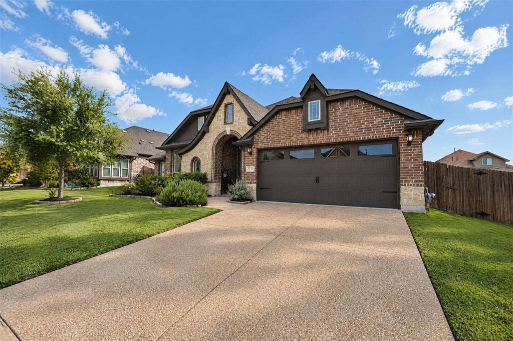 3210 Creekhaven Drive, Melissa, TX 75454 Exterior elevation featuring a combination of brick and stone veneer, a multi-gabled roofline, a multi-car garage with glass panels, and an aggregate concrete driveway