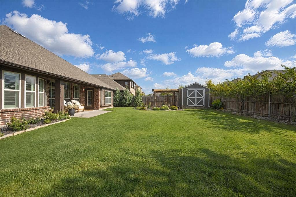 3210 Creekhaven Drive, Melissa, TX 75454 Expansive backyard featuring a concrete patio, manicured lawn, wooden perimeter fencing, detached storage shed, and a pergola