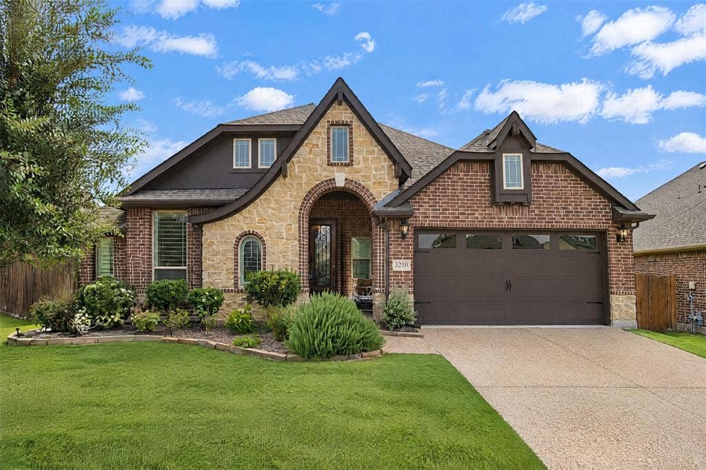 3210 Creekhaven Drive, Melissa, TX 75454 Multi-gabled exterior featuring brick and stone masonry, a covered arched entryway, arched window accents, and a dual-bay garage