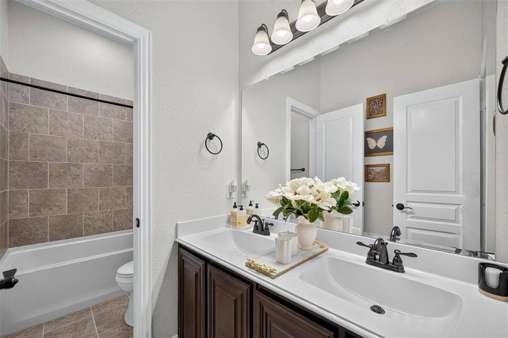 3210 Creekhaven Drive, Melissa, TX 75454 Double vanity featuring a light-toned countertop, rectangular undermount sinks, dark wood-finish cabinetry, and matte black fixtures
