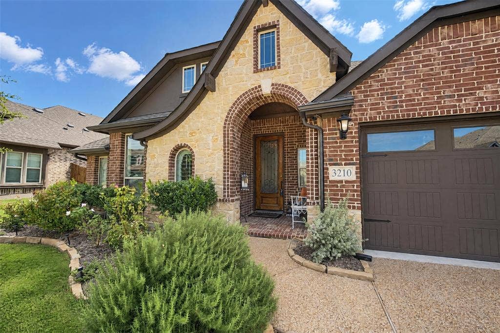 3210 Creekhaven Drive, Melissa, TX 75454 Stone and brick facade featuring an arched entryway, decorative wood front door with glass inlay, and an attached multi-car garage with carriage-style detailing