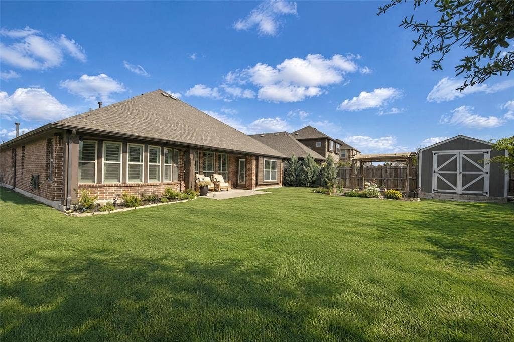 3210 Creekhaven Drive, Melissa, TX 75454 Backyard featuring a brick-exterior residence, a concrete patio, a wood-framed pergola, and a detached storage structure