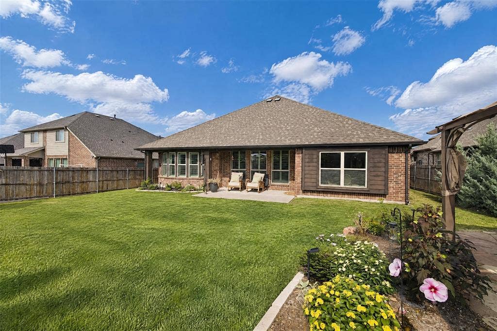 3210 Creekhaven Drive, Melissa, TX 75454 Brick exterior featuring a concrete patio, wood-style trim accents, and a fenced backyard with landscaped garden beds