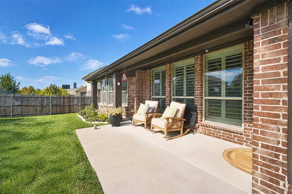 3210 Creekhaven Drive, Melissa, TX 75454 Covered concrete patio featuring brick exterior siding, plantation-style window shutters, and a fenced backyard with lawn