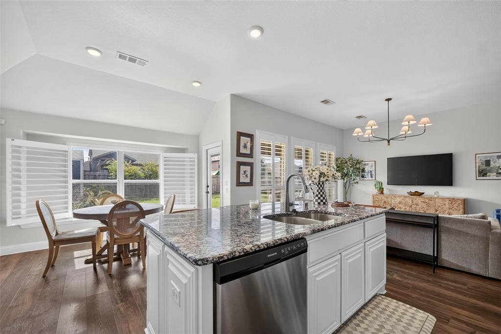 3210 Creekhaven Drive, Melissa, TX 75454 Kitchen island featuring a stone-look countertop, undermount sink, and stainless steel dishwasher, vaulted ceilings, wood-finish flooring, and white plantation shutters