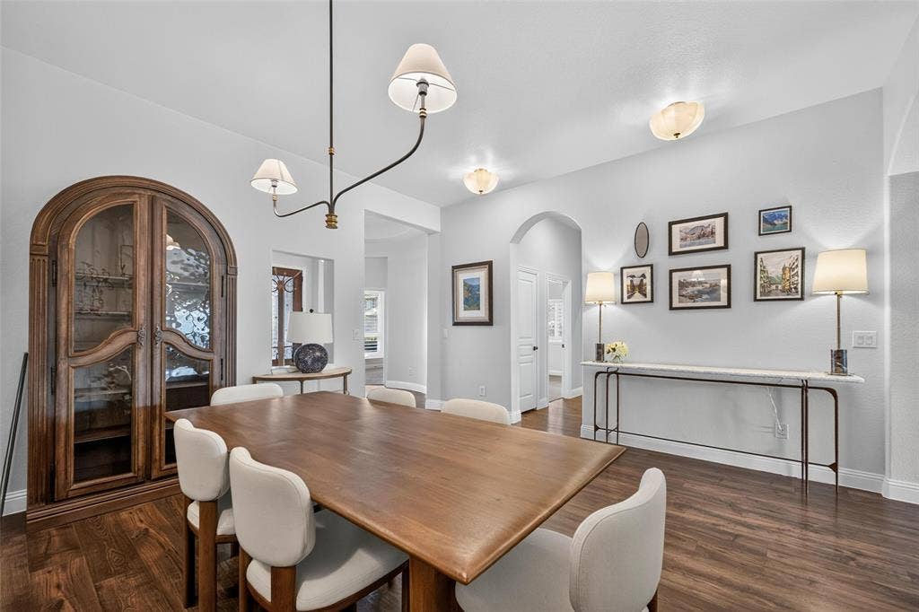 3210 Creekhaven Drive, Melissa, TX 75454 Dining area featuring wood-finish flooring, an arched doorway, and a built-in arched wooden display cabinet with glass shelving