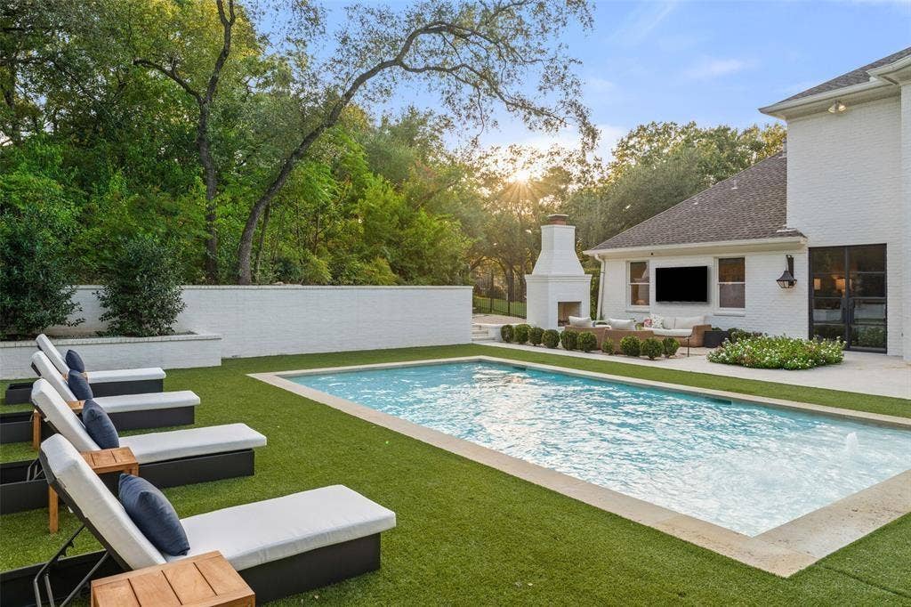 4201 Green Cliffs Road, Austin, TX 78746 Outdoor living area featuring a rectangular swimming pool, artificial turf surround, an outdoor fireplace, and a white brick exterior