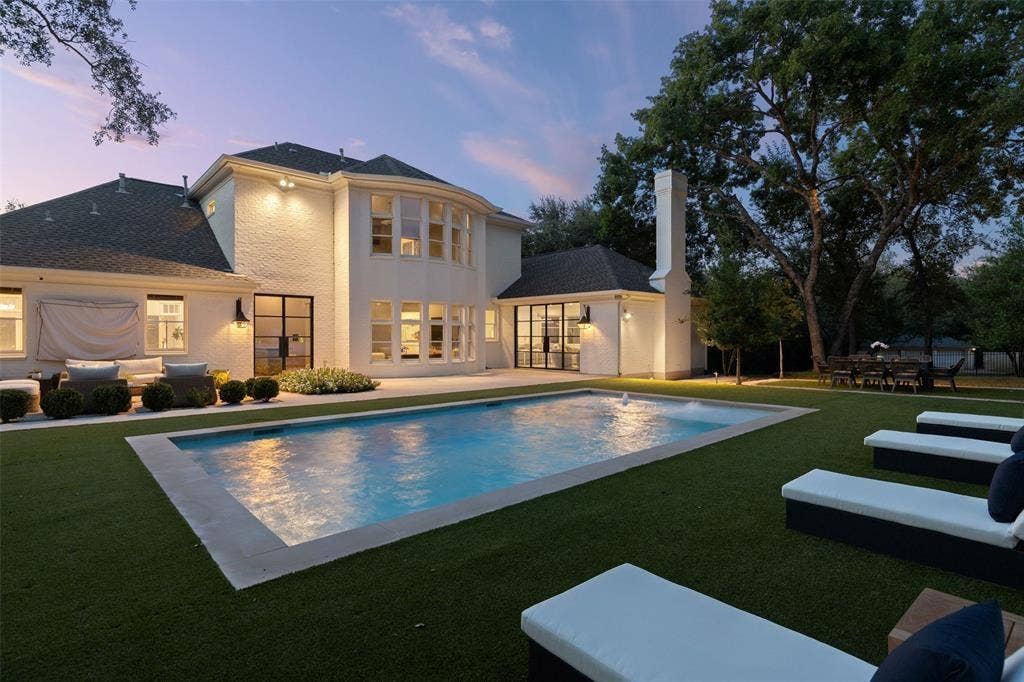 4201 Green Cliffs Road, Austin, TX 78746 White brick exterior, rectangular swimming pool, expansive artificial turf lawn, mature trees, and a tall exterior chimney